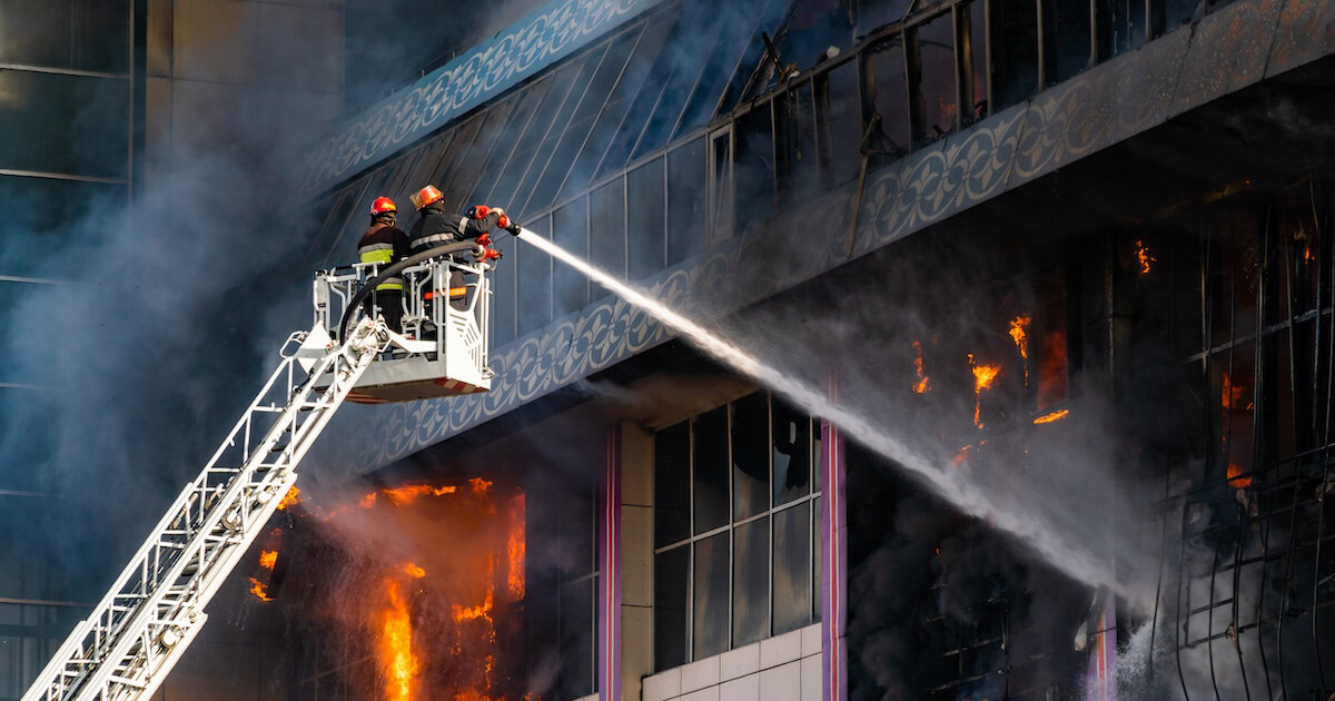 A firefighter on aerial apparatus sprays water into a burning high-rise building.