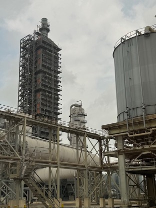 Carbon capture use and storage infrastructure including piping in the foreground and towers and stacks in the background.