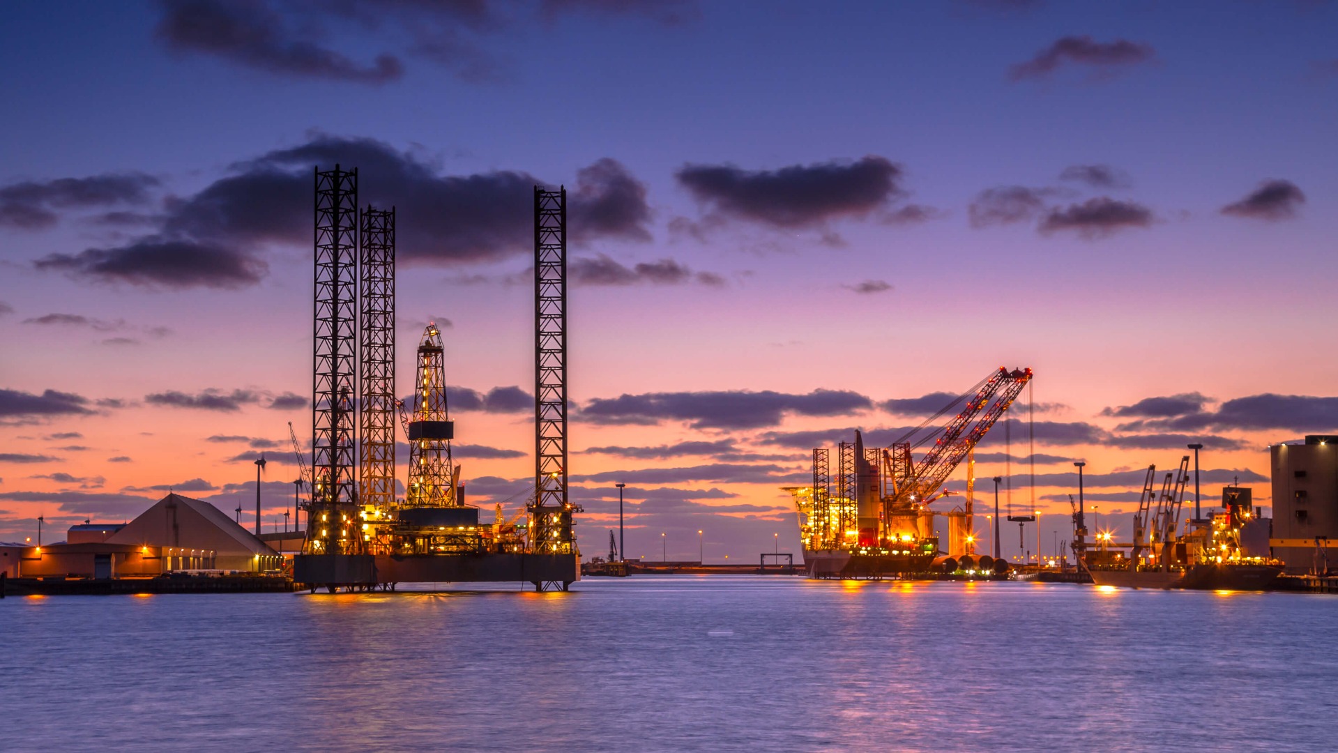 Offshore oil drilling equipment consisting of tall steel structures seen at dusk.