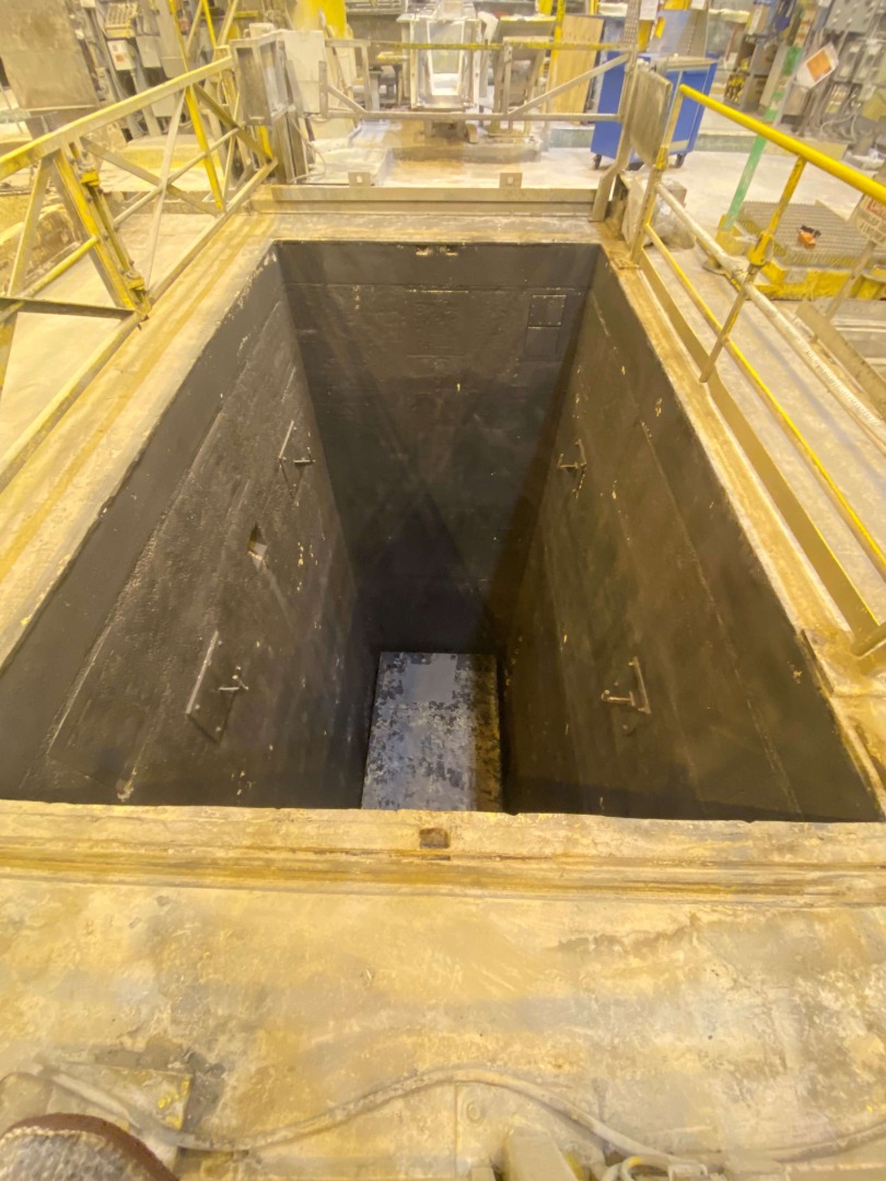 An overview of a deep, narrow concrete pit used in the aluminum casting process.